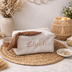 Trousse de rangement personnalisée en velours côtelé couleur lin, avec nœud décoratif et fermeture zippée, posée sur un support en fibres naturelles